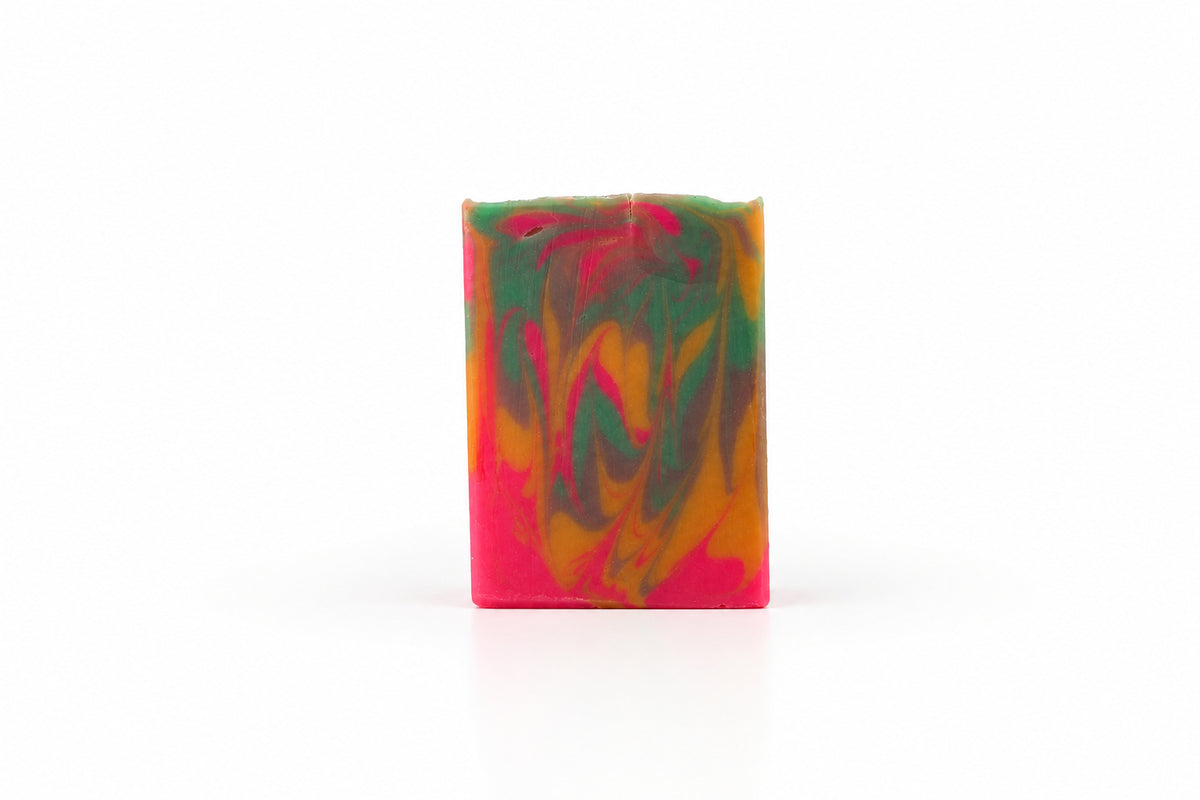 A rectangular handmade soap bar with a marbled swirl pattern of pink, green, and orange, standing upright on a white surface against a white background.