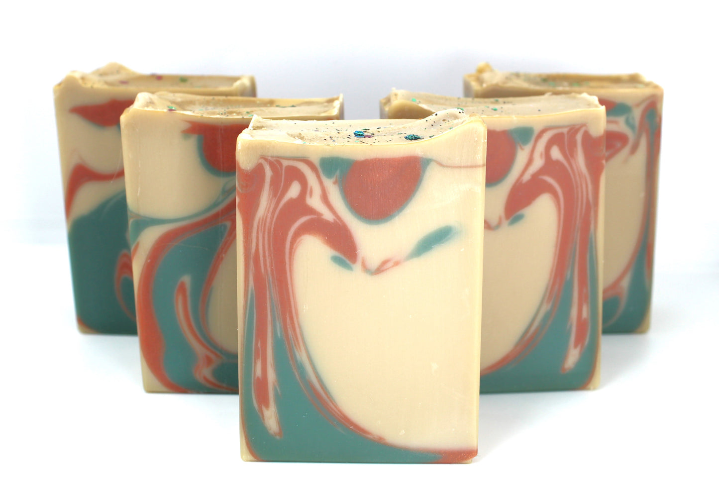 Staggered bars of tan colored soap with copper and green swirls on white background.