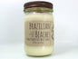 White wax candle in a mason jar with a rustic brown metal lid. Kraft brown label with black text. White background.