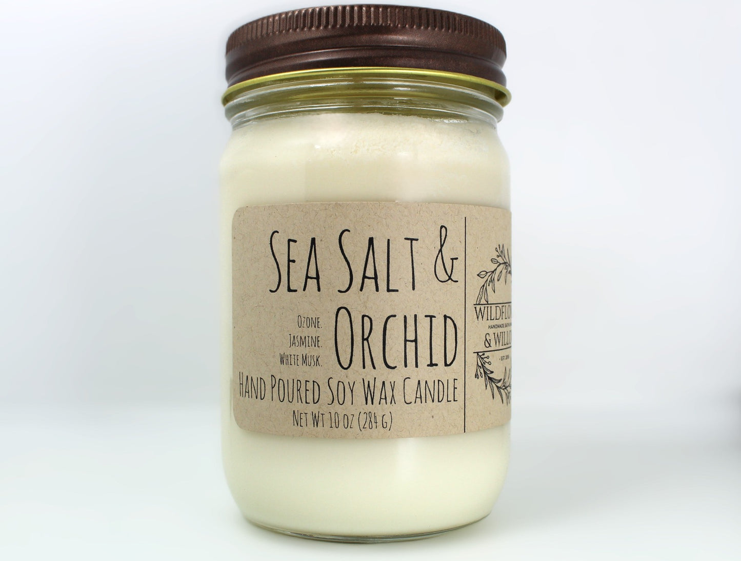 White wax candle in a mason jar with a rustic brown metal lid. Kraft brown label with black text. White background.