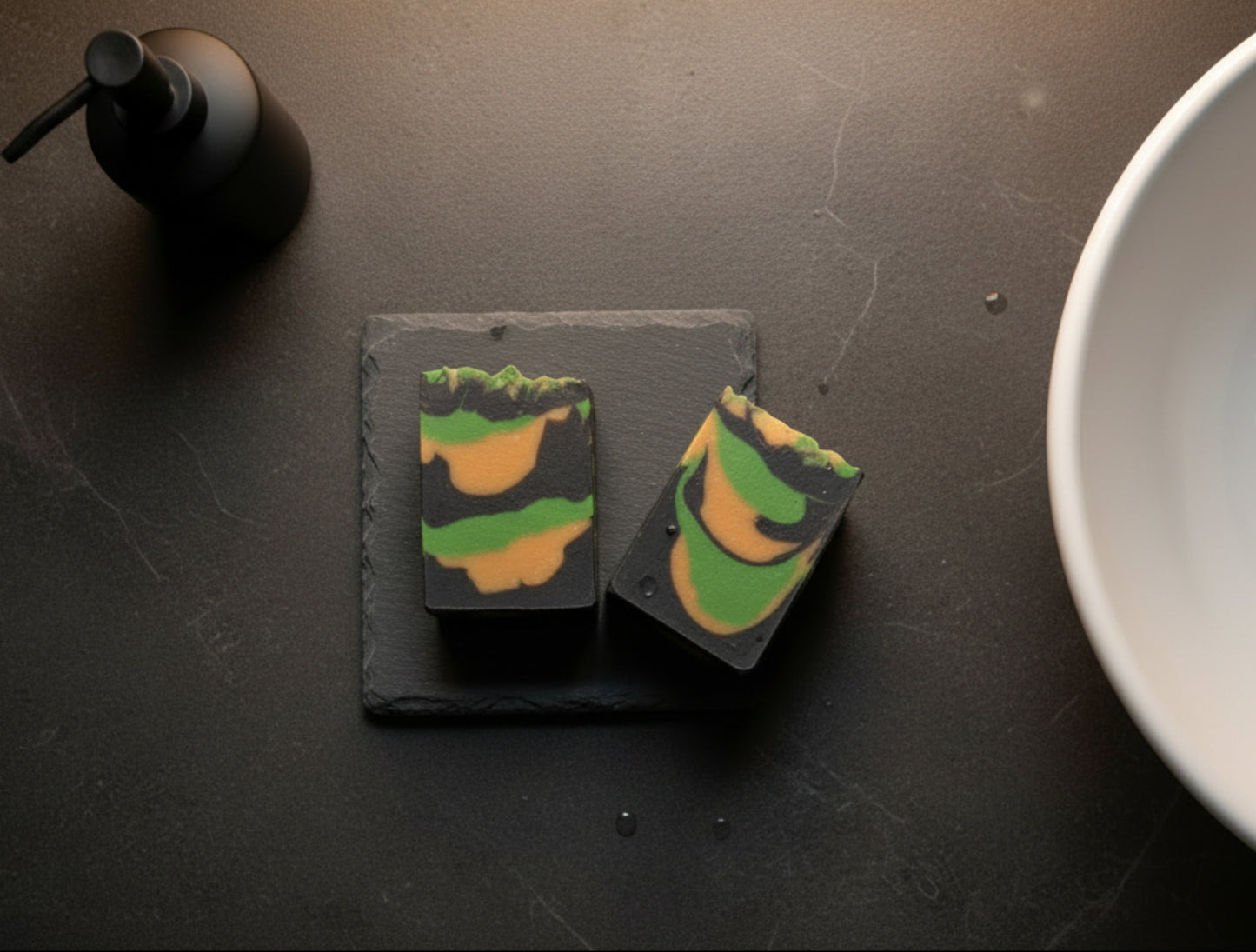 Two handmade bars of soap in a bathroom near a sinnk on a slate soap dish