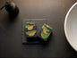 Two handmade bars of soap in a bathroom near a sinnk on a slate soap dish