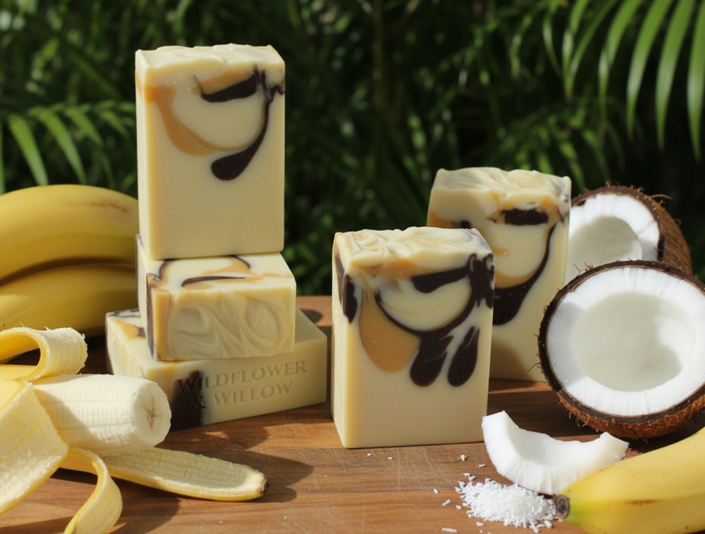 Five handmade rectangular bars of soap with a cream base and dark brown and yellow swirls, displayed on a board surrounded with bananas and coconuts