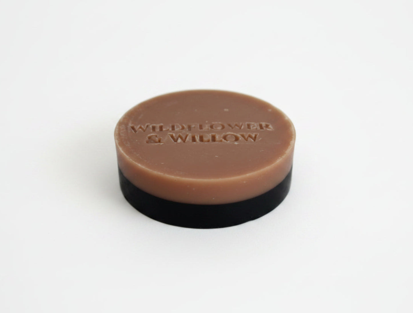 A round bar of soap with a pink top layer and a black base, photographed on a plain white background.