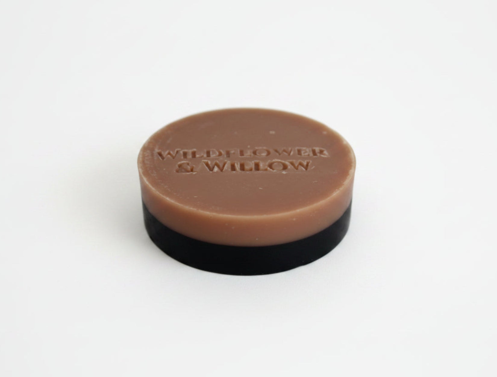 A round bar of soap with a pink top layer and a black base, photographed on a plain white background.