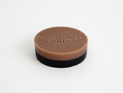 A round bar of soap with a pink top layer and a black base, photographed on a plain white background.