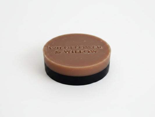 A round bar of soap with a pink top layer and a black base, photographed on a plain white background.