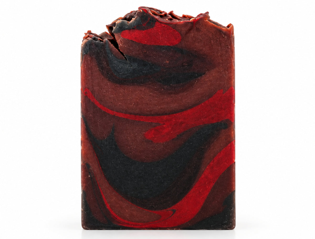 A rectangular bar of handmade soap with a swirled pattern of dark brown, black, and red, standing upright on a white surface against a white background.